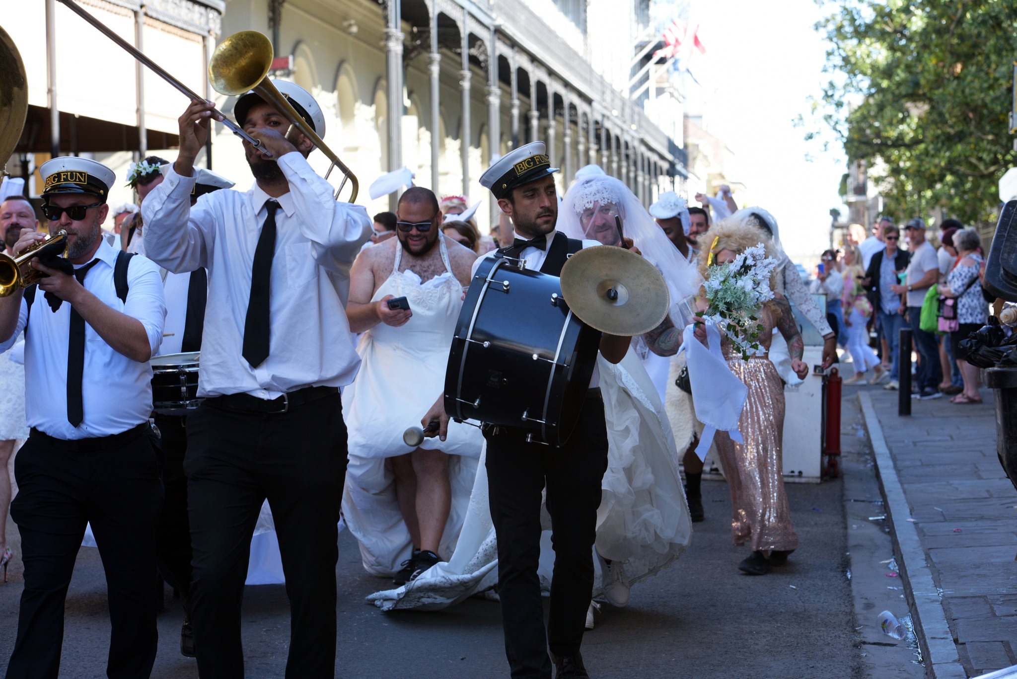 This image shows a brass band leading a group of people dressed as brides