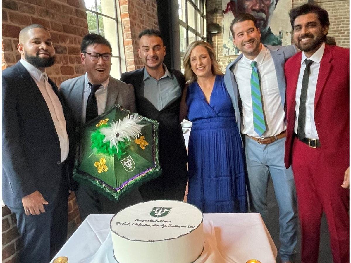Recent graduates standing behind a graduation cake