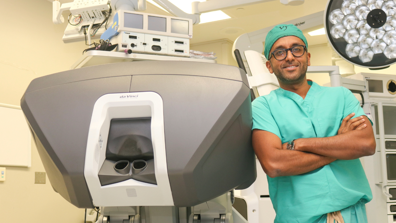This is a picture of Dr. Adarsh Vijay next to a surgical robot.