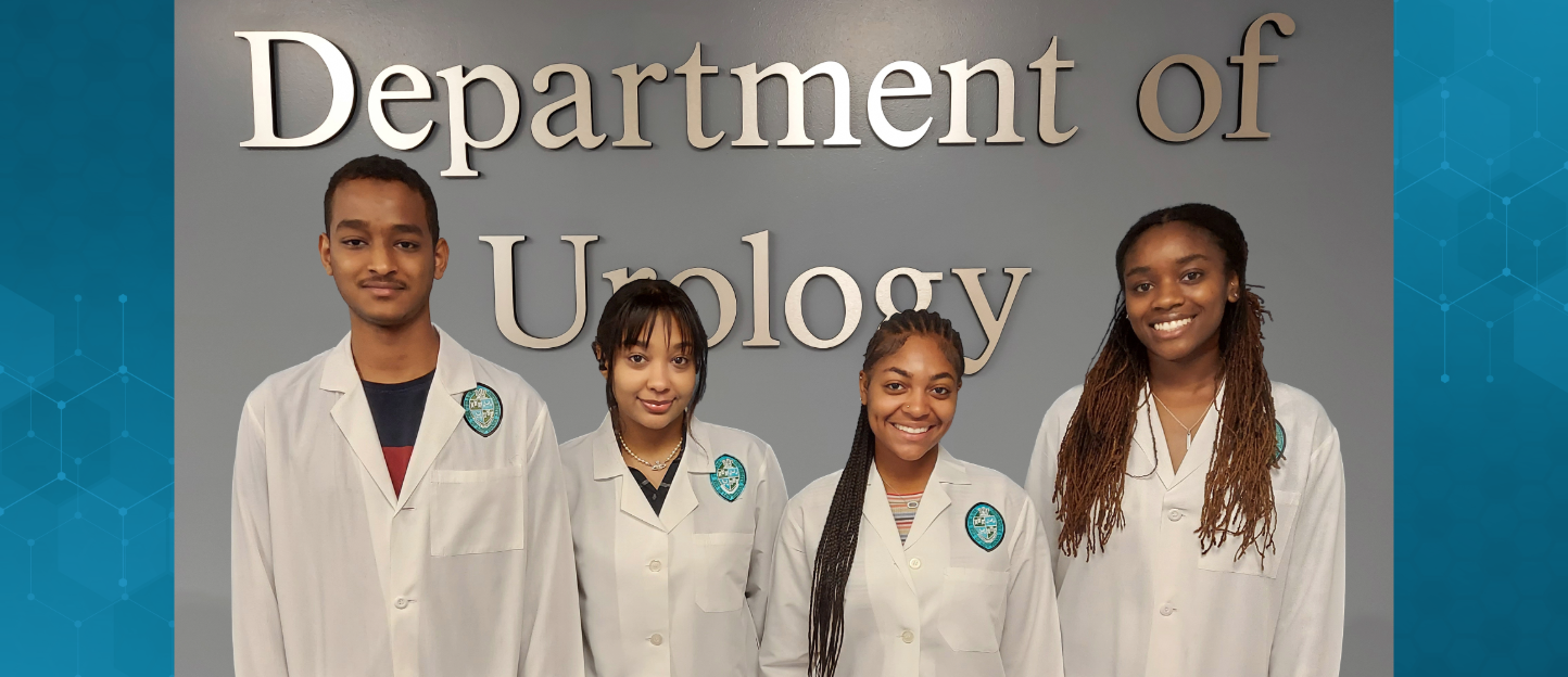 This picture shows four students in white doctors coats in front of a Department of Urology sign