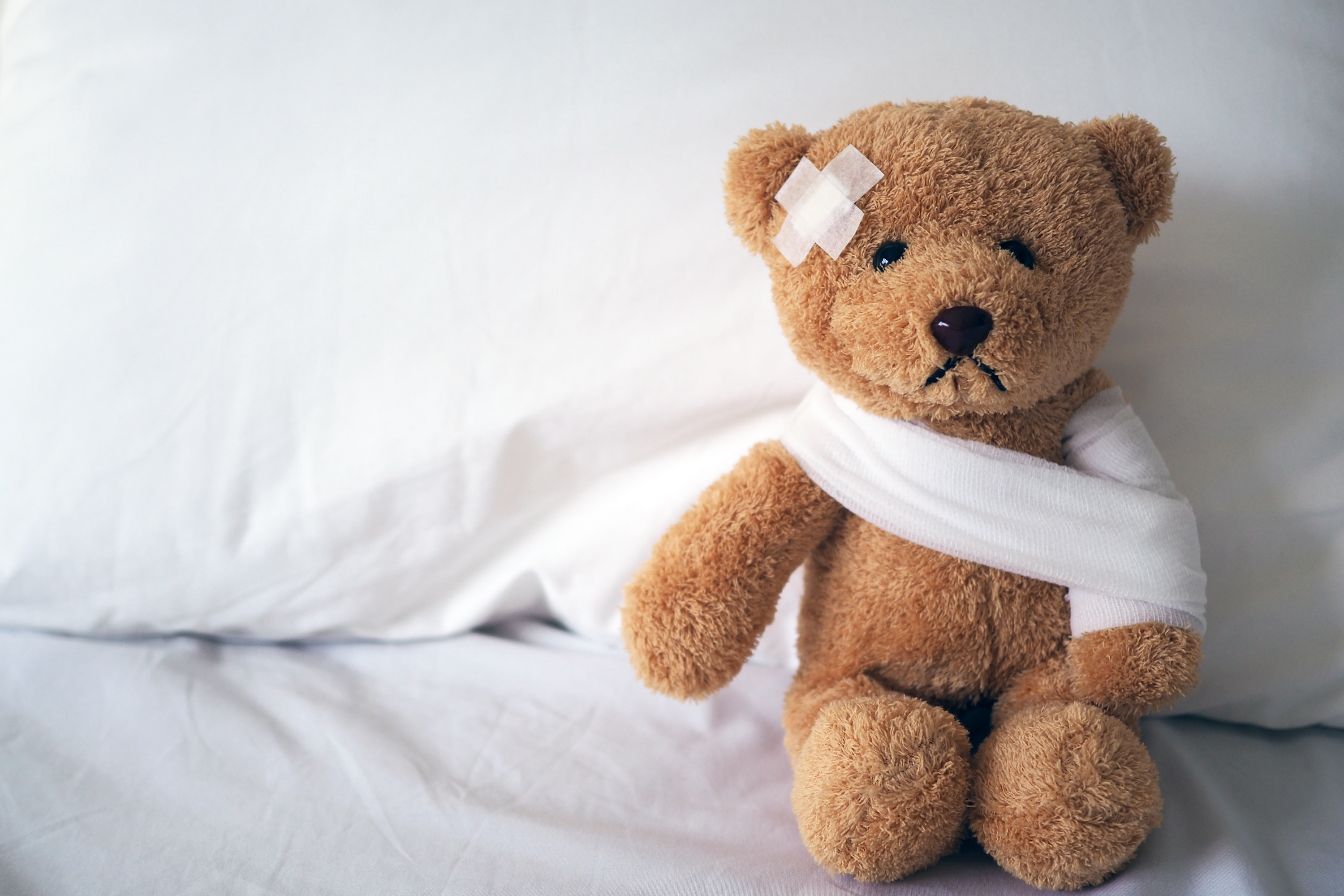 This photo shows a bandaged up and frowning teddy bear in a hospital bed