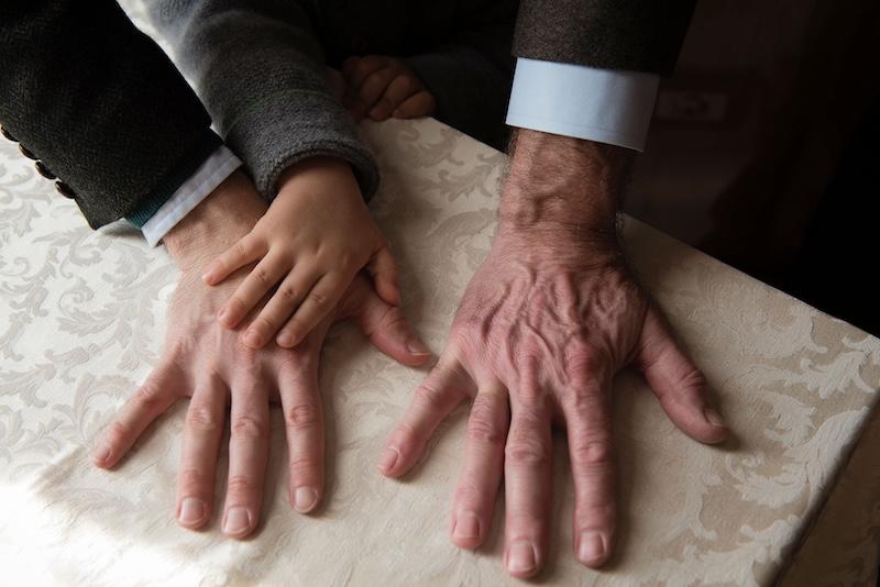 Three right hands on a table, one of an elderly hand, one of a middle-aged hand, and a child's hand