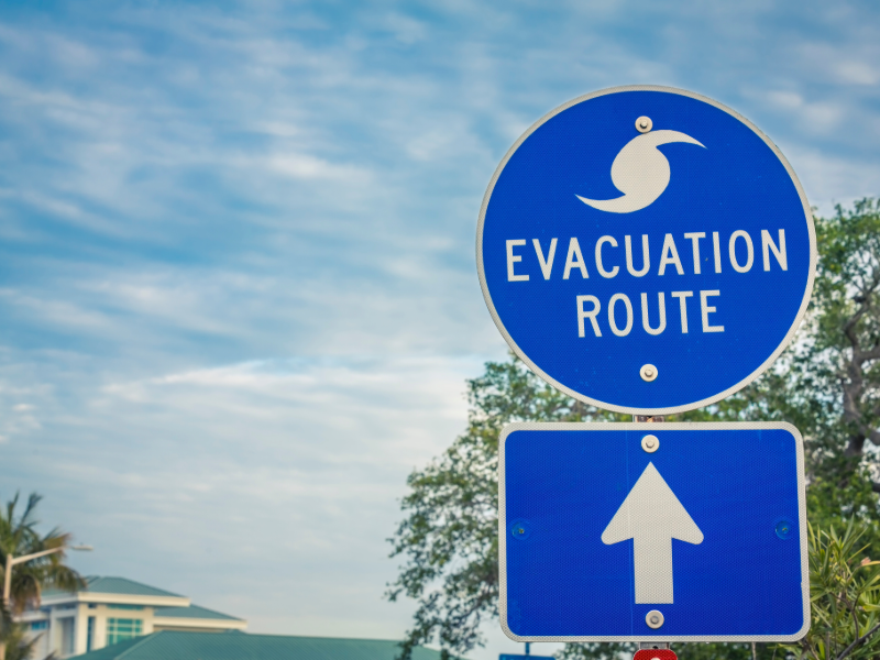 A blue evacuation route sign with a cloudy sky behind it