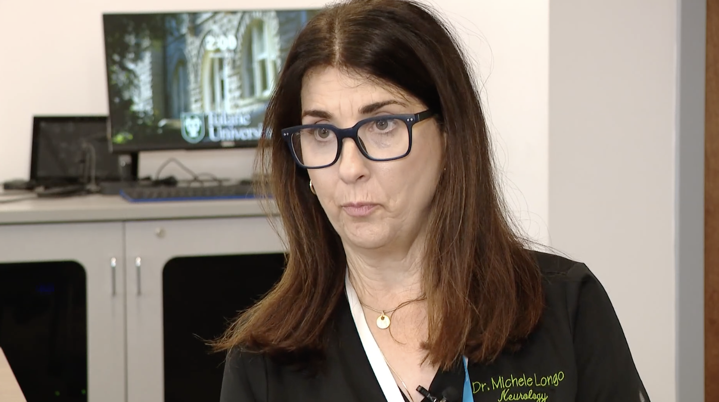 A woman with brown hair wearing glasses and a black jacket in a TV interview