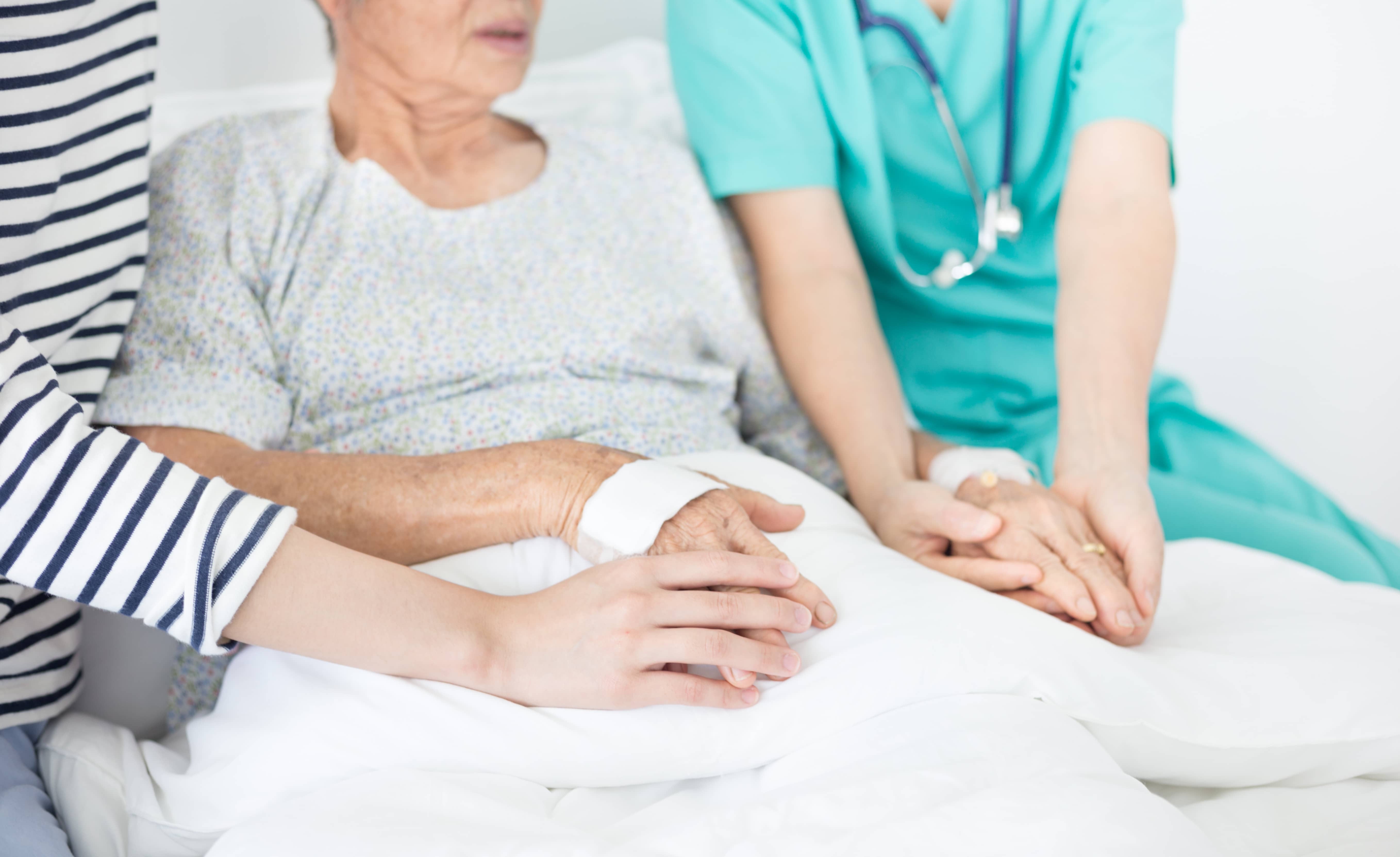 a medical professional and a family member hold hands with an elderly person