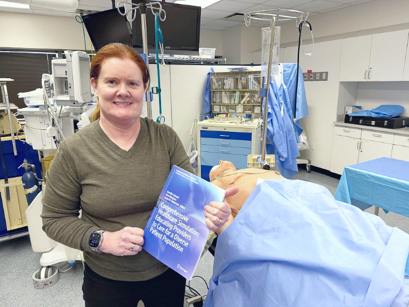 Jennifer Calzada holds the textbook she edited in front of a medical simulator