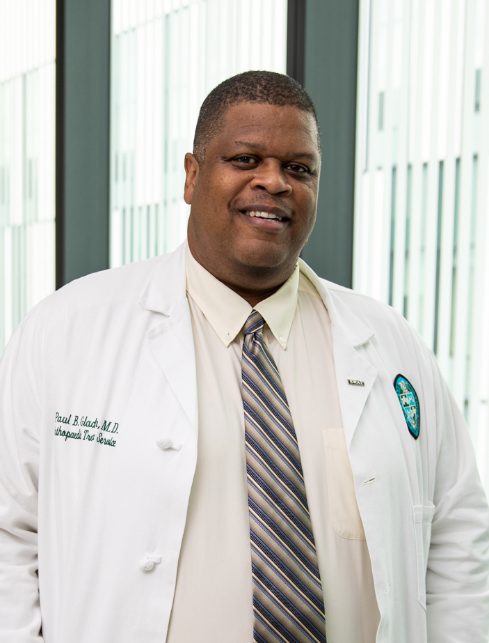 Photograph: Smiling Black man in white lab coat, tan shirt, and striped tie.