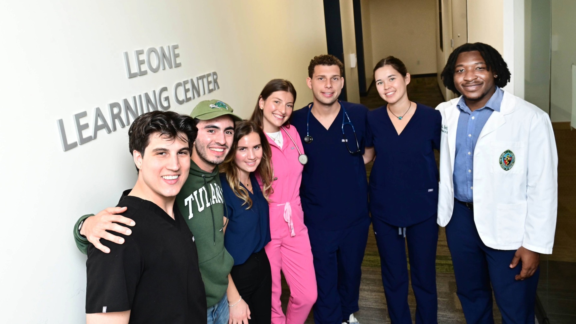 A group of people, some wearing medical scrubs and one wearing a short white doctors' coat stand in front of a sign that says Leone Learning Center