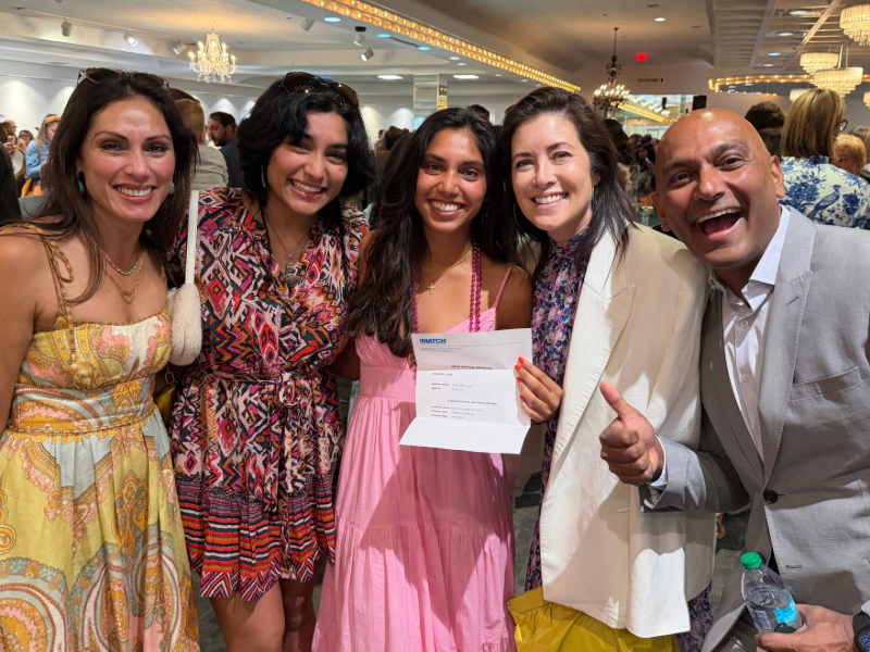 A group of people stands smiling and hugging and one is holding a match letter