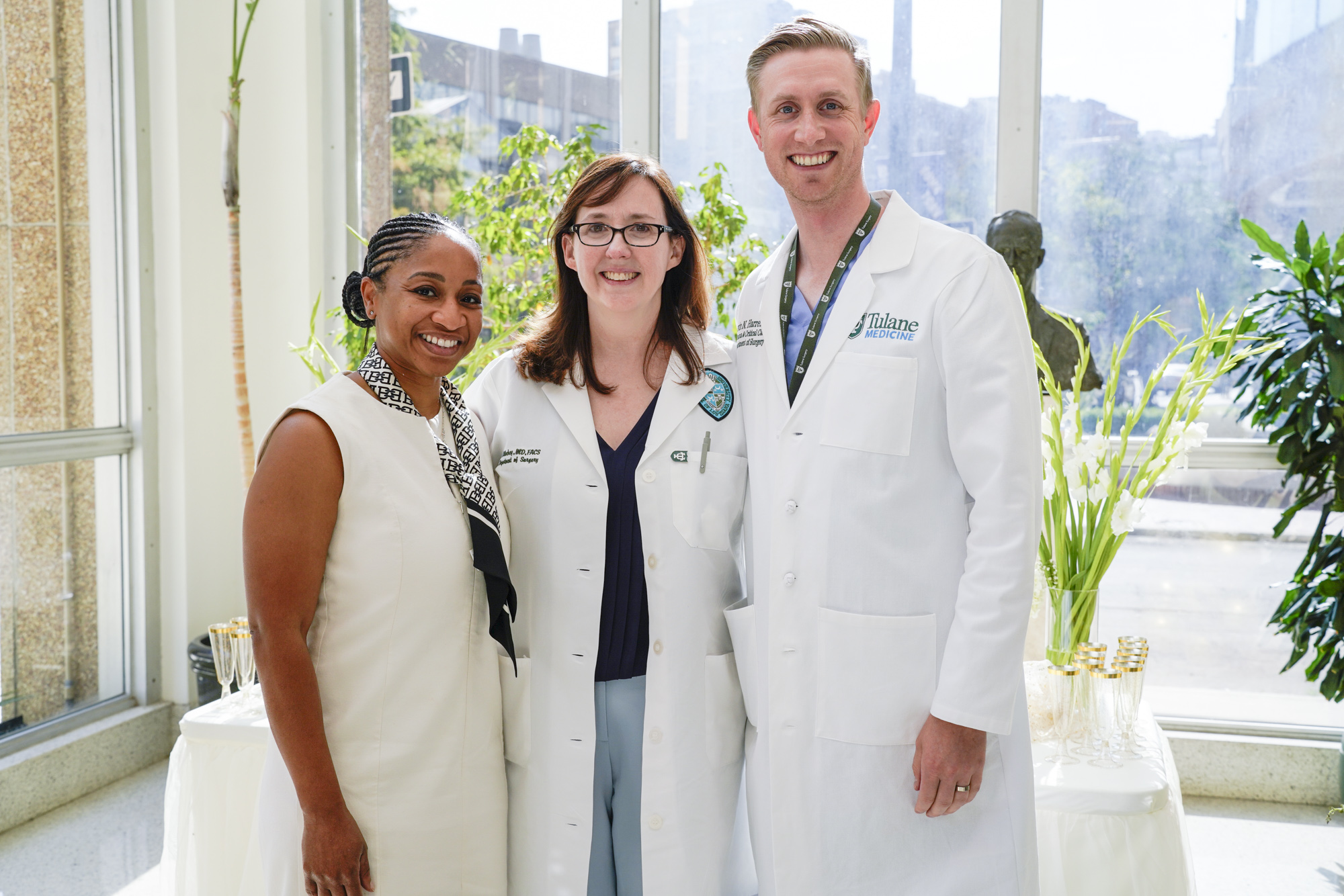 Photograph of three smiling healthcare professionals posing together in a bright lobby.