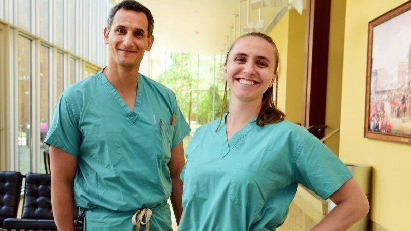 Two smiling healthcare workers wearing teal scrubs in a bright hospital lobby.