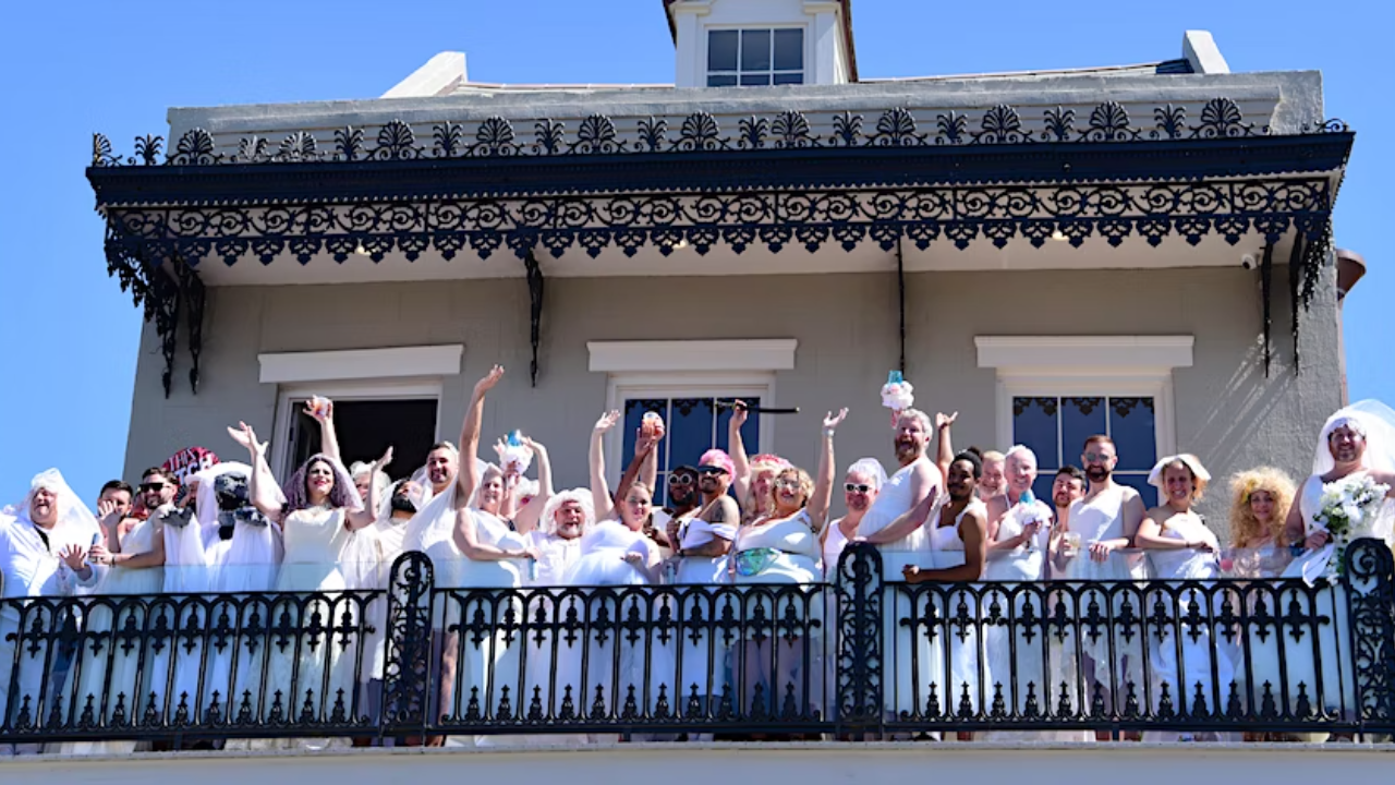 This image shows a group of people wearing wedding dresses standing on a balcony