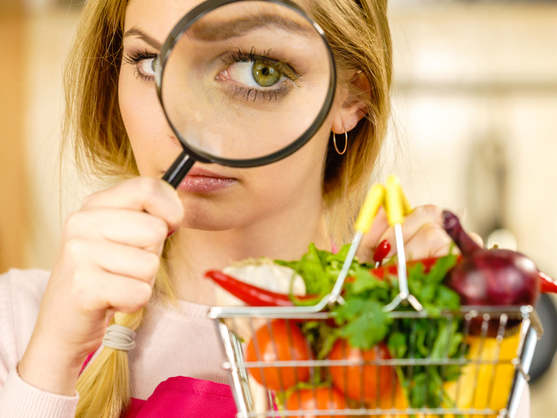 This image shows a woman holding a magnifying glass and looking at a basket of produce