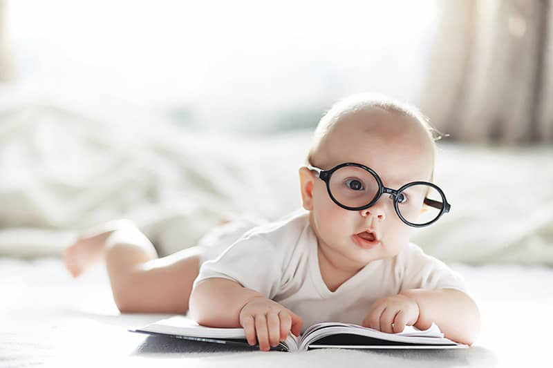 infant wearing glasses looking at a book