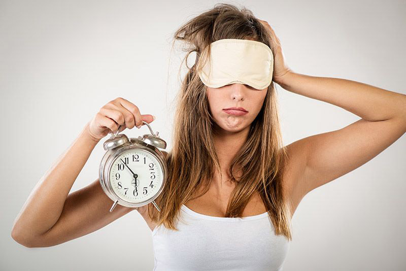woman wearing sleep mask and holding alarm clock