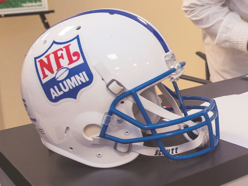 A white football helmet sitting on a table. The helmet has the NFL Alumni logo on it