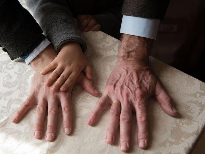 Three right hands on a table, one of an elderly hand, one of a middle-aged hand, and a child's hand