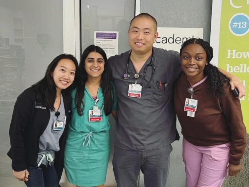 Four people in medical scrubs posing with their arms around each other