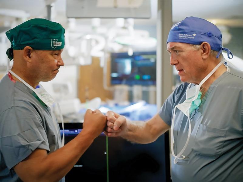 Two physicians in medical scrubs bump fists in a clinical setting