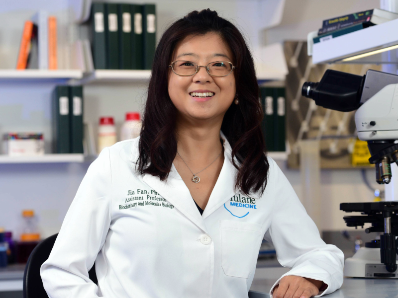 A woman wearing a white lab coat is standing next to a microscope in a laboratory