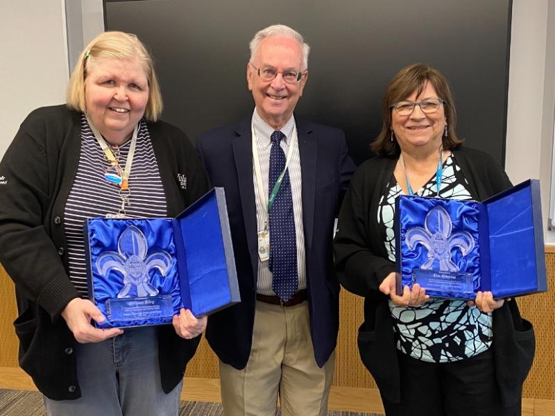Two women hold awards in blue cases with a man standing between them