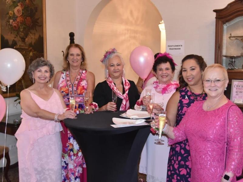 A group of women dressed in pink stand around a table
