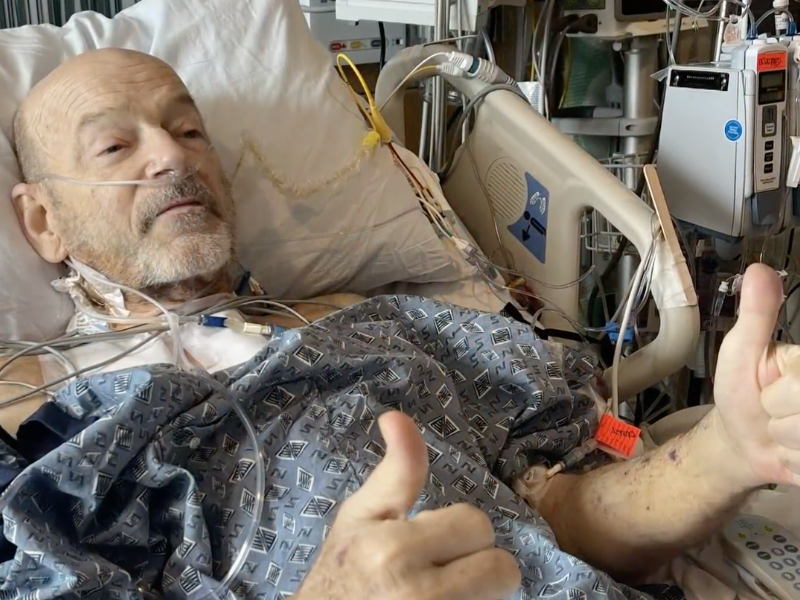 A man in a hospital bed gives two thumbs up