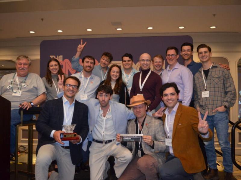 Large group smiling, holding trophies and peace signs at an awards event.