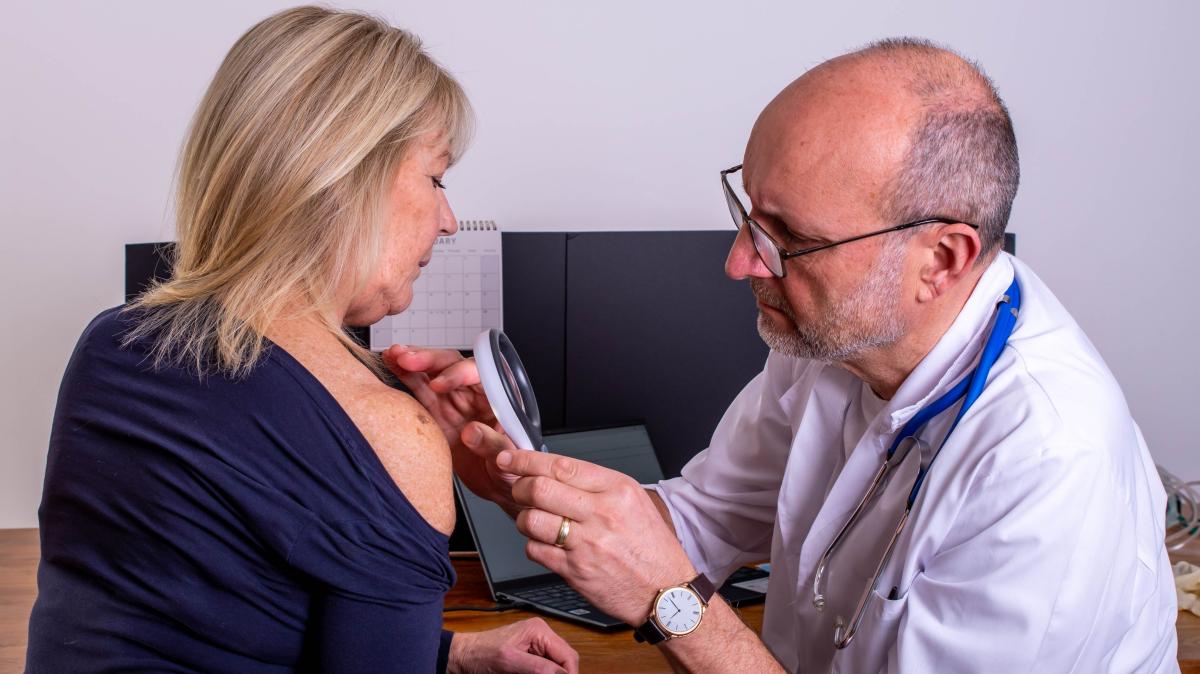 Dermatologist examines a mole on a woman's shoulder with a dermatoscope.
