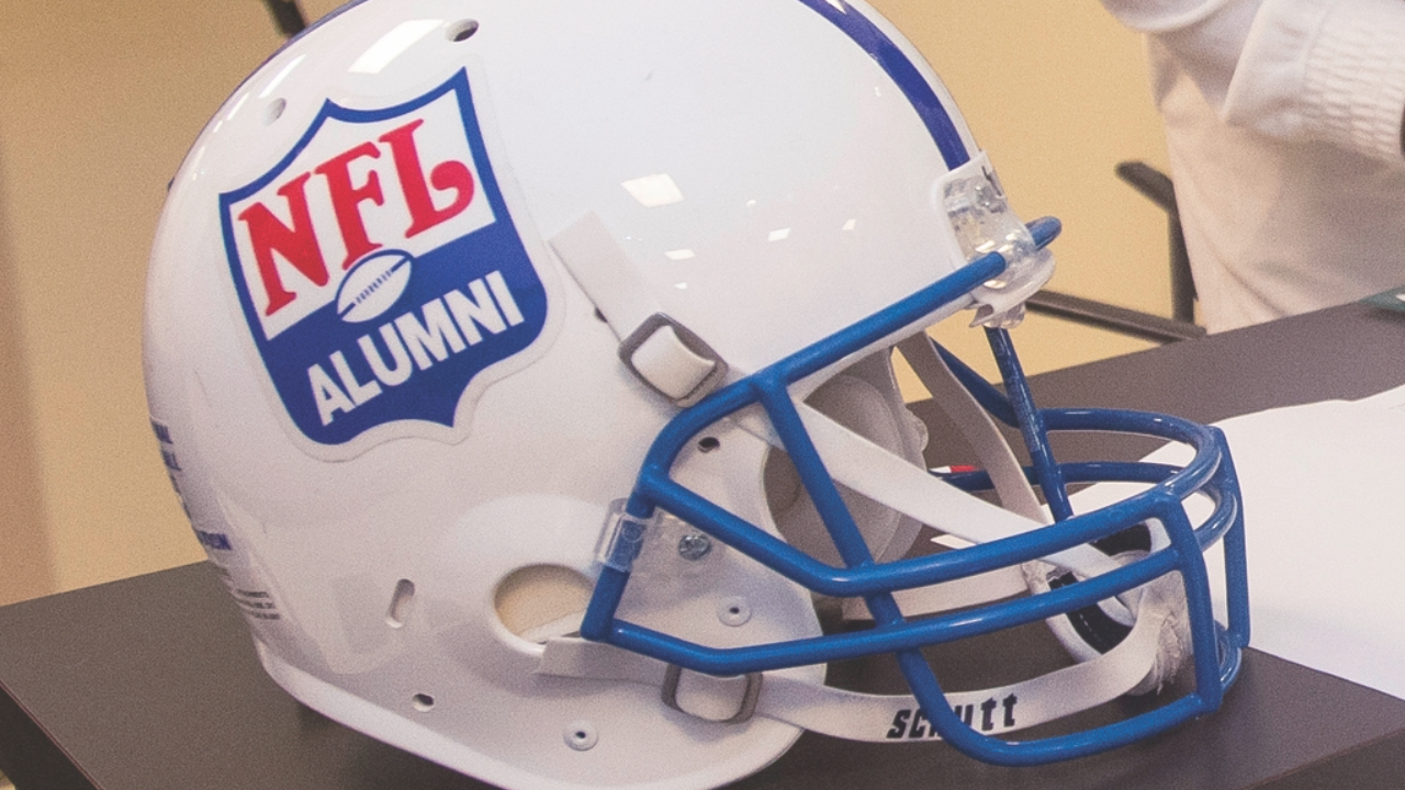 A white football helmet sitting on a table. The helmet has the NFL Alumni logo on it