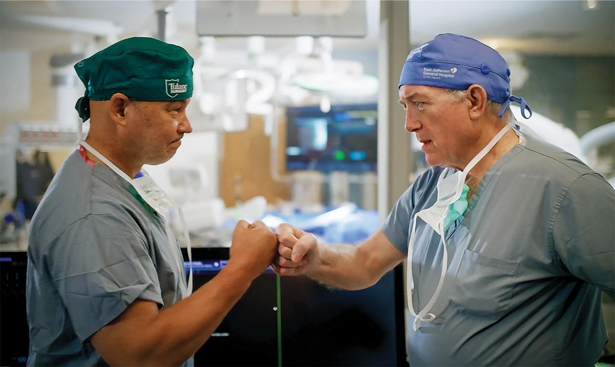 Two physicians in medical scrubs bump fists in a clinical setting