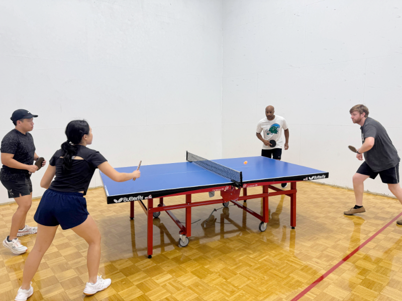 Four people play ping pong on a blue table 