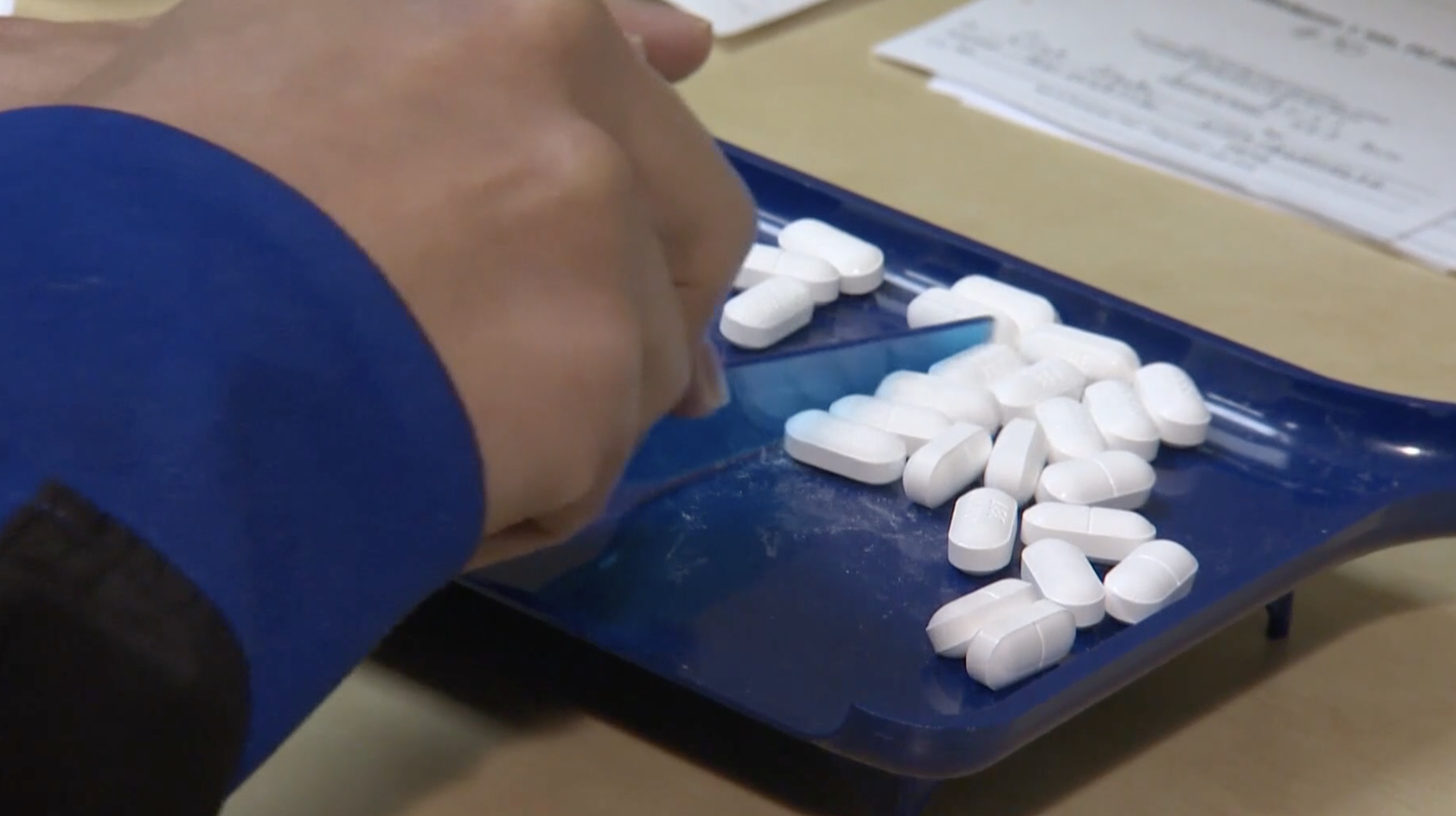 A hand sorts pills on a blue tray