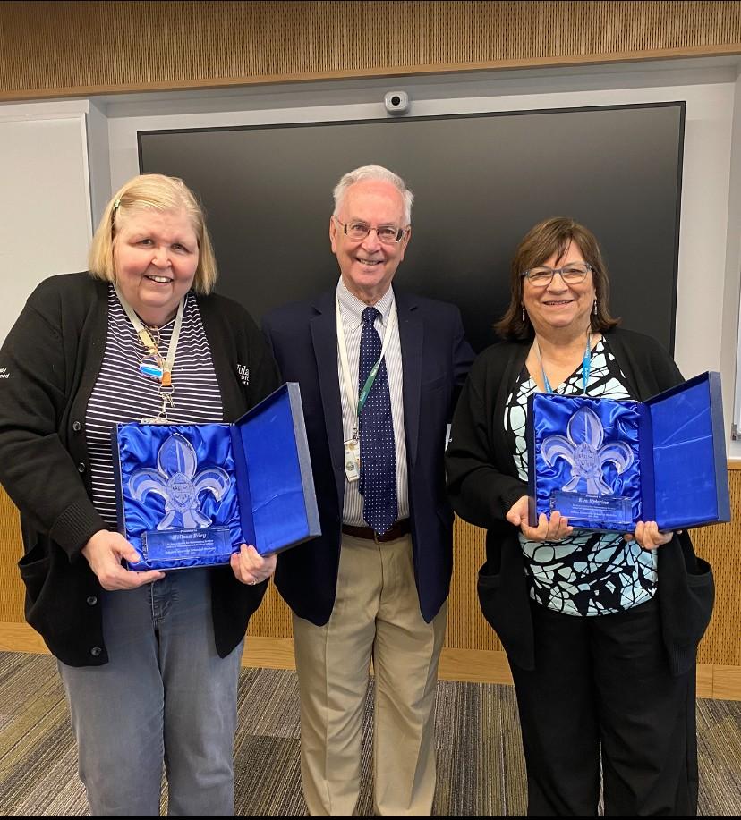 Two women hold awards in blue cases with a man standing between them