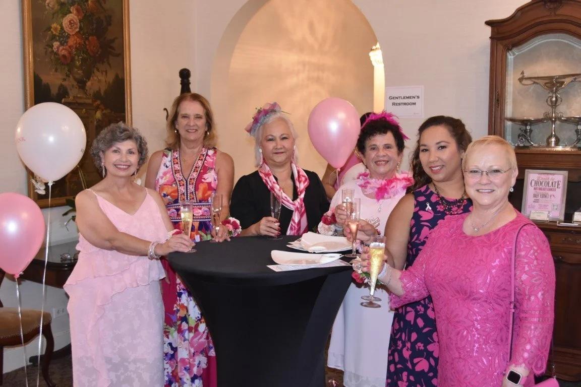 A group of women dressed in pink stand around a table