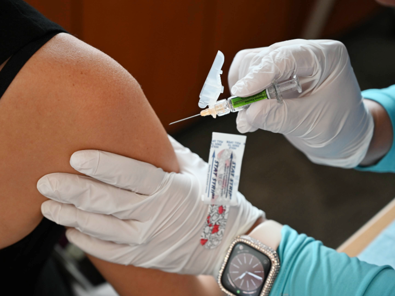 Gloved hands holding a flu vaccine are holding an arm about to receive the shot