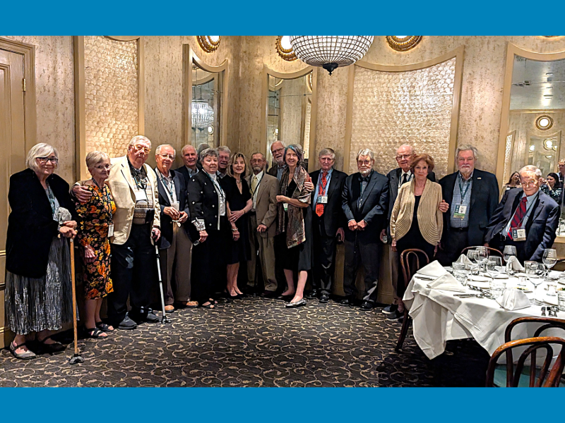 A group of elderly men and women stand in an ornately decorated room