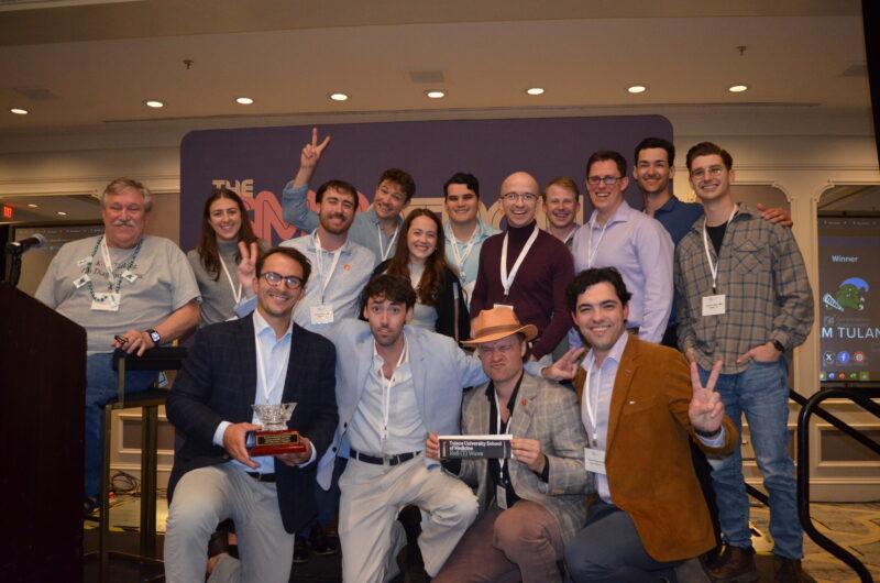Large group smiling, holding trophies and peace signs at an awards event.