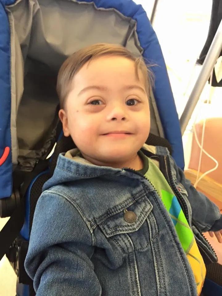 Smiling child in a blue stroller, wearing a denim jacket.