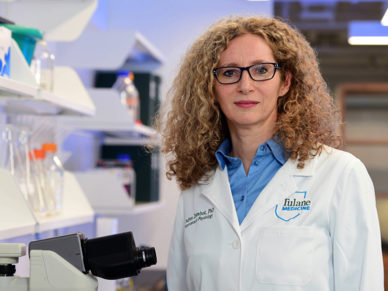 A portrait of Andrea Zsombok in a lab. She is wearing a blue shirt under a white lab coat