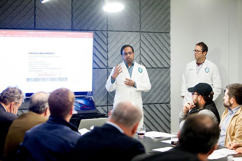 Two physicians in white coats talk to a room full of students
