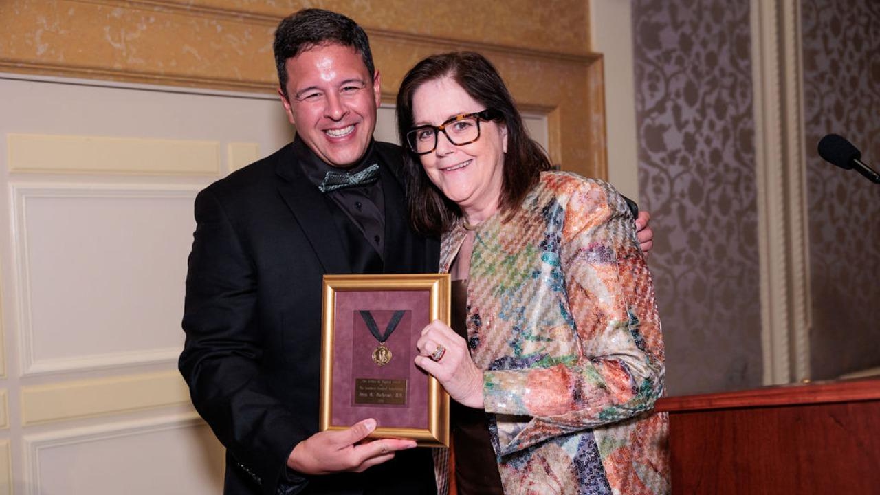 This image shows a smiling man receiving an award from a smiling woman.