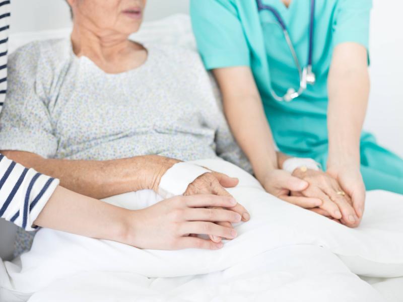 a medical professional and a family member hold hands with an elderly person