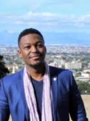 Photo depicts Fungai in a navy blue blazer, smiling and looking off into the distance. 