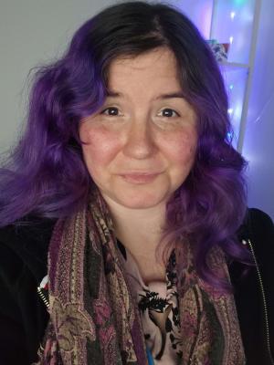 Close-up of a smiling woman with wavy purple hair and a patterned scarf.